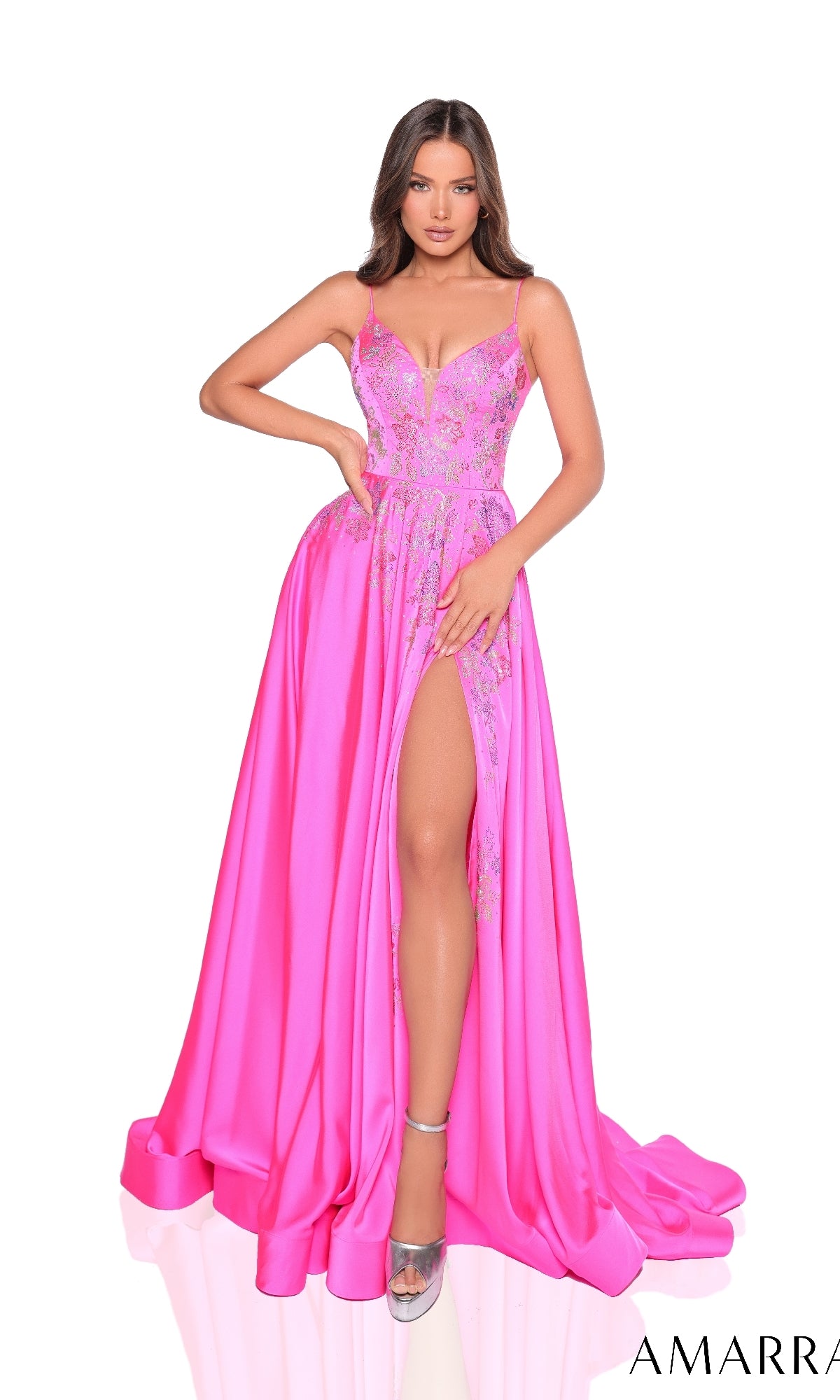 A woman wearing the Amarra 88354 long prom dress in bright pink, featuring lace detailing, a deep neckline, and a high slit, poses with one hand on her hip.